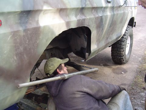 1990 Ford Bronco - A person works on the wheel well of a camouflage SUV, likely a 1990 Ford Bronco, during a repair.