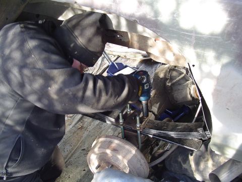 1990 Ford Bronco - Mechanic tightens U-bolts on leaf spring suspension system with an impact wrench.