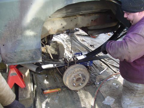 1990 Ford Bronco - Mechanic works on the suspension system of a vehicle, focusing on the leaf springs and axle.