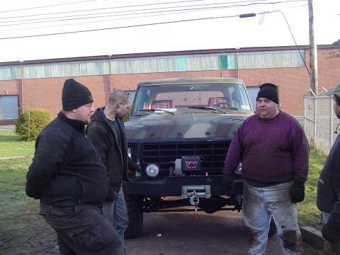 1990 Ford Bronco - A camouflage Ford truck with a winch is parked outside, with three men gathered around it.