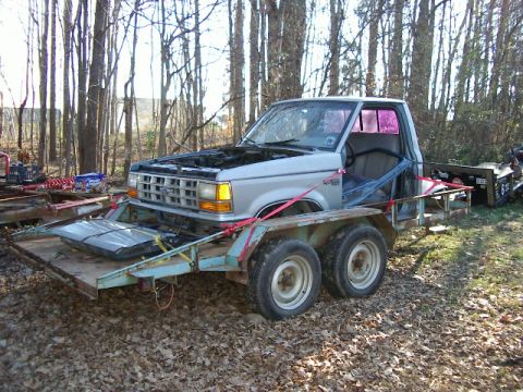 1985 Ford Bronco - Silver Ford Ranger pickup truck on a trailer, hood open, in a wooded area.