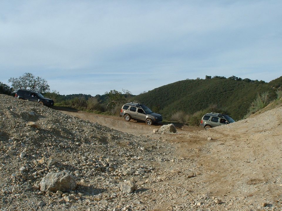 Three SUVs driving on a rocky, off-road trail with hills in the background