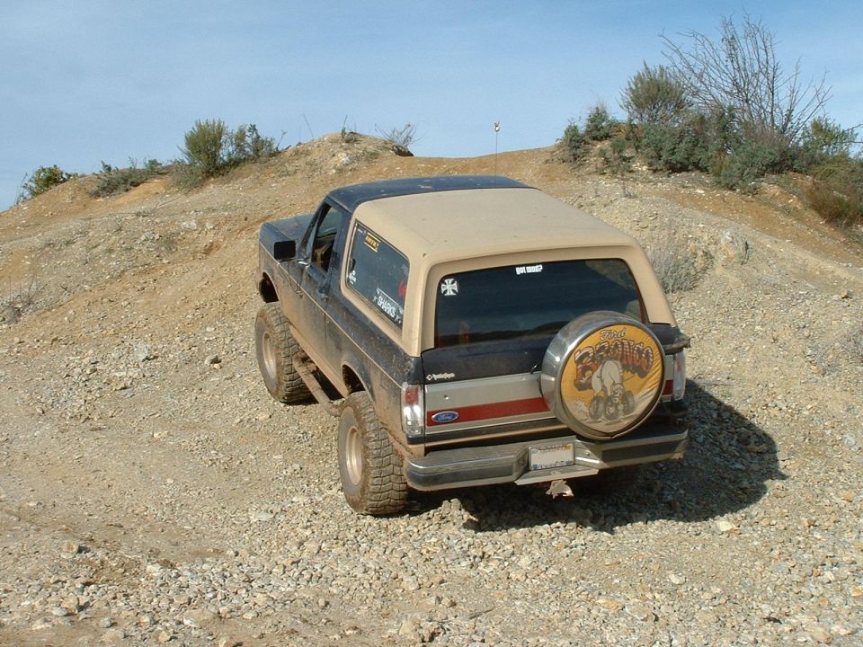 Black and tan Ford Bronco with a spare tire cover, driving on a dirt road