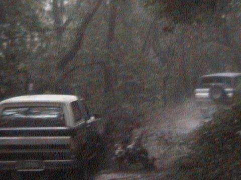 1990 Ford Bronco - Two SUVs navigate a muddy path through a wooded area.