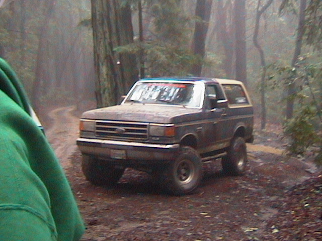 1990 Ford Bronco driving on a muddy forest road