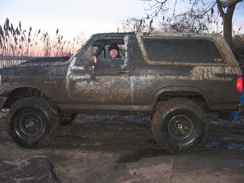Mud-covered SUV, side view, with a person inside, off-road tires, in a muddy field