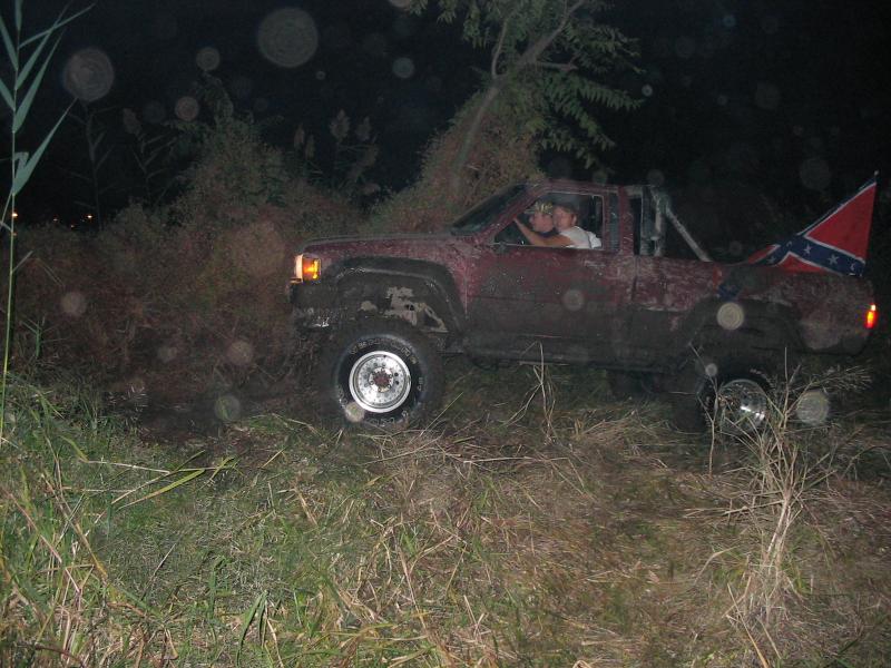 Red pickup truck with Confederate flag flying from the bed, seen from the side at night