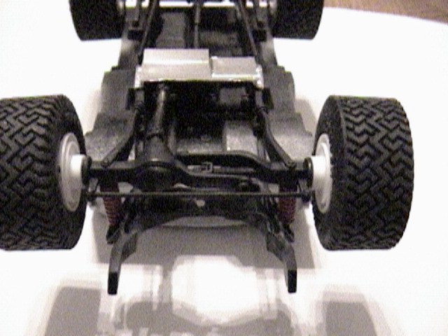 Underside of scale model truck chassis showing front axle, coil springs and white wheels