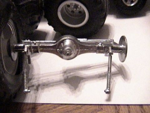 1979 Ford Bronco - A chrome-plated model-kit rear axle assembly laid on white paper, showing the pumpkin-shaped differential housing, axle tubes, brake backin…