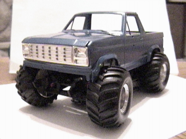 Blue Ford Bronco scale model built as a monster truck with oversized tires, posed on white paper