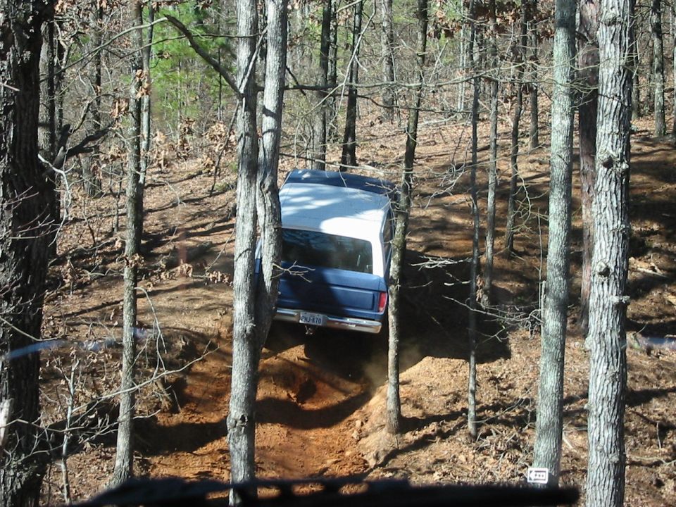 1978 Ford Bronco driving on a dirt path through trees