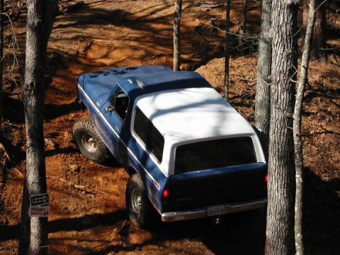1978 Ford Bronco - A blue and white 1978 Ford Bronco navigates a wooded, off-road trail.