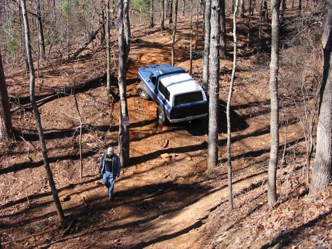 1978 Ford Bronco - A person walks down a wooded trail as a blue and white SUV navigates the terrain above.