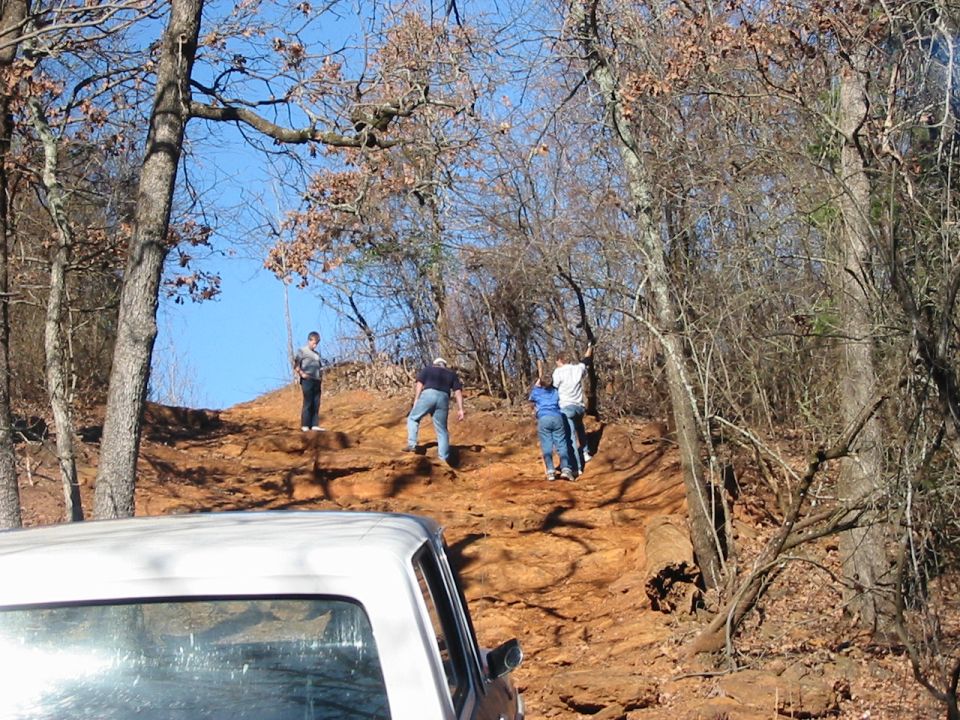 White pickup truck front corner, parked on a dirt hill with people walking up