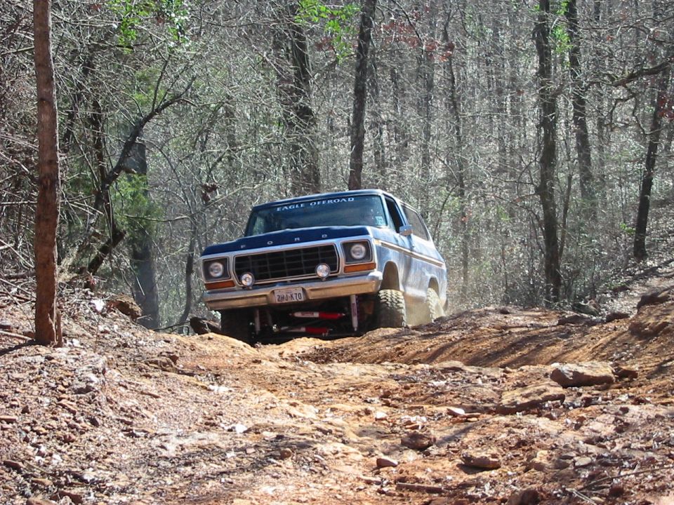 1978 Ford Bronco climbing a dirt trail in woods, 'EAGLE OFFROAD' sticker on windshield