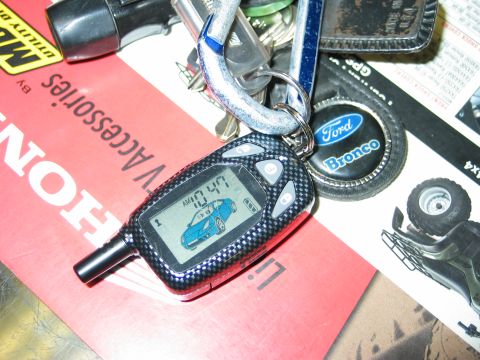1995 Ford Bronco - Key fob and Ford Bronco emblem on a keychain, resting on various papers and accessories.