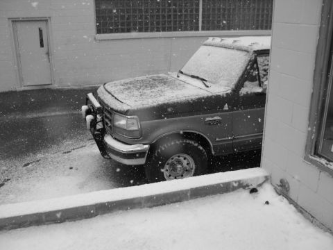 1995 Ford Bronco - A Ford truck is parked in a snowy lot next to a building with a glass block window.