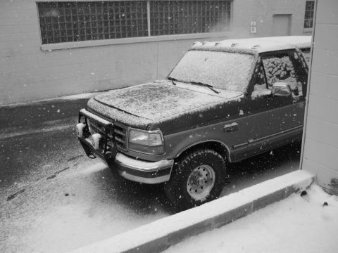 1995 Ford Bronco - A Ford Bronco sits parked on a snowy street, partially obscured by falling snow.