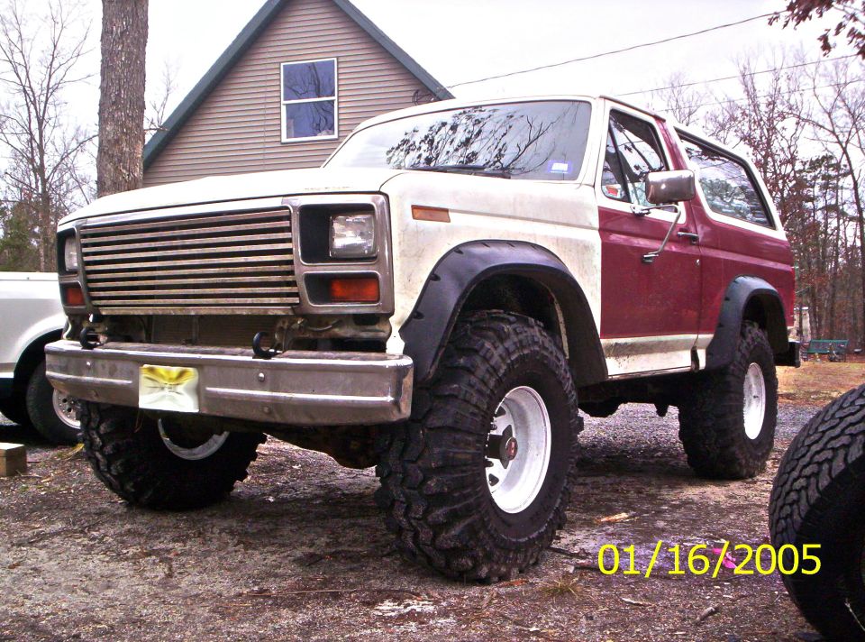 Lifted red and white full-size Ford Bronco on mud tires parked by a house, dated 01/16/2005
