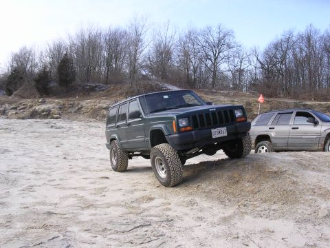 1995 Jeep Cherokee - Two SUVs navigate a sandy, off-road terrain with trees in the background.