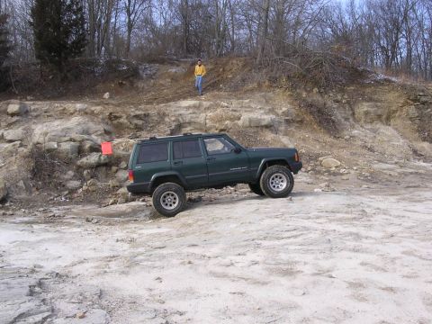 1995 Jeep Cherokee - A green 1995 Jeep Cherokee navigates a rocky, off-road trail with a person standing on a hill in the background.