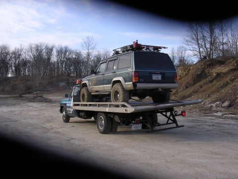 1995 Jeep Cherokee - Jeep Cherokee being towed on a flatbed truck, showing its rear profile and roof rack.
