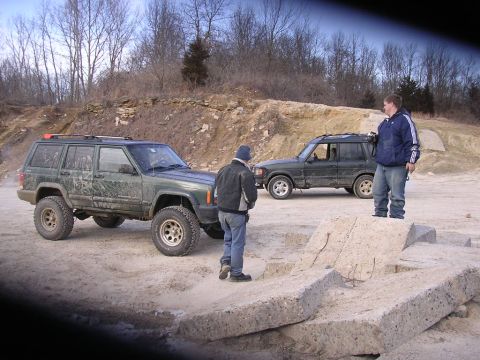 1995 Jeep Cherokee - Two SUVs are parked on a dirt lot with men standing around them.