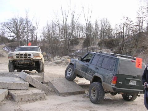 1995 Jeep Cherokee - Two modified SUVs navigate an off-road obstacle course with concrete blocks.