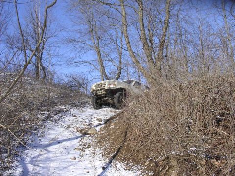 1995 Jeep Cherokee - A white SUV tackles a challenging snowy path through a wooded area.