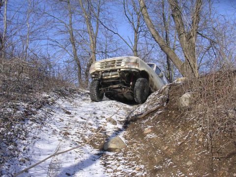 1995 Jeep Cherokee - Ford Bronco navigating a challenging off-road path with snow and dirt.