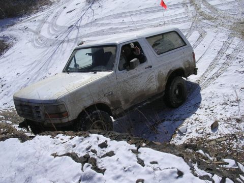 1995 Jeep Cherokee - White Ford Bronco navigating a difficult snowy and muddy off-road course.