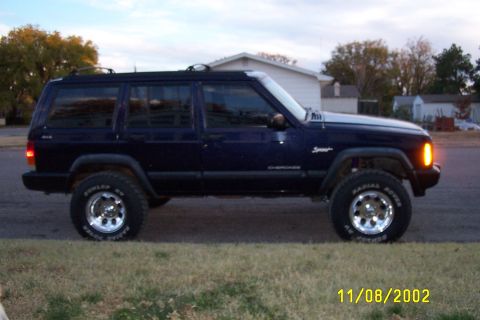 1998 Jeep Cherokee - A dark blue Jeep Cherokee Sport is parked on the side of the road with a residential area in the background.