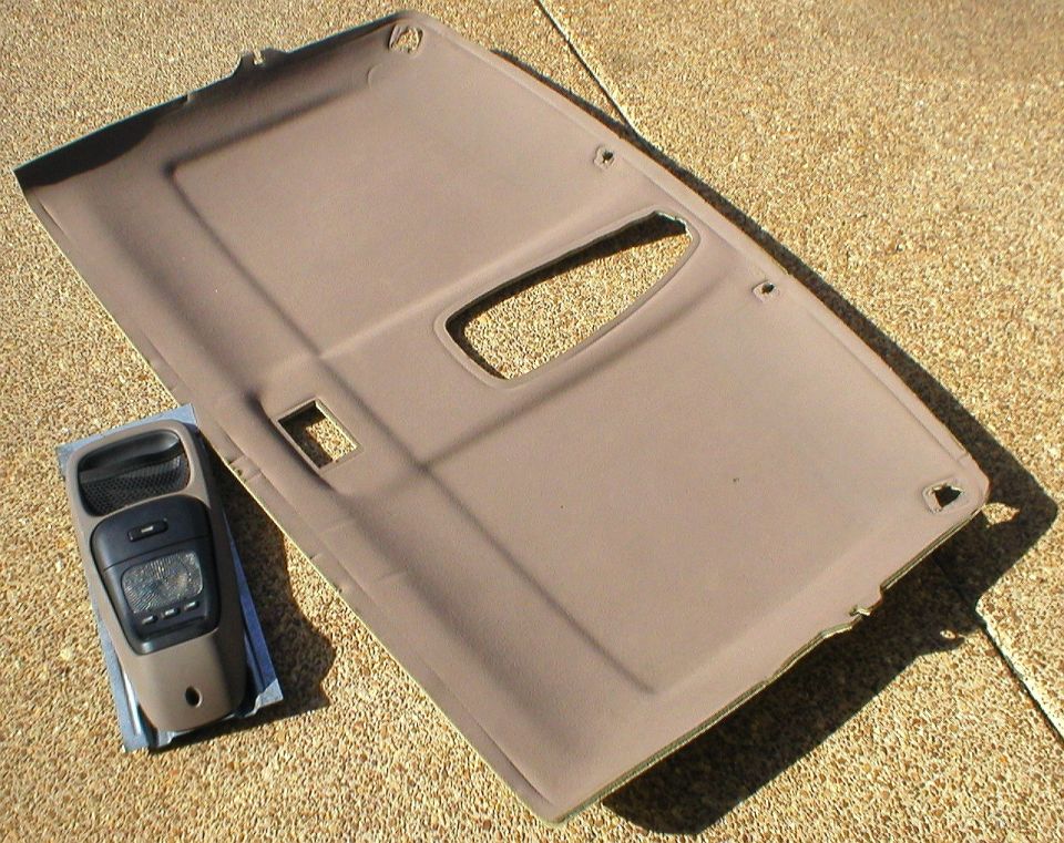 Tan vehicle headliner panel laid on driveway beside a removed gray overhead console