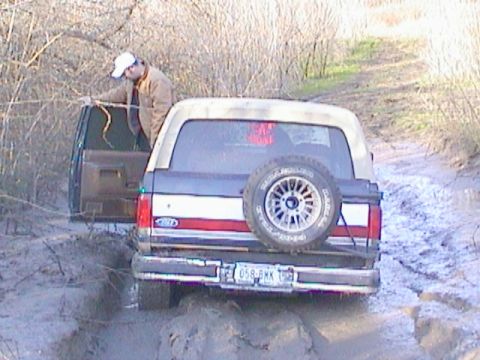 1989 Ford Bronco - A 1989 Ford Bronco is stuck in the mud on a trail, with another vehicle partially visible behind it.