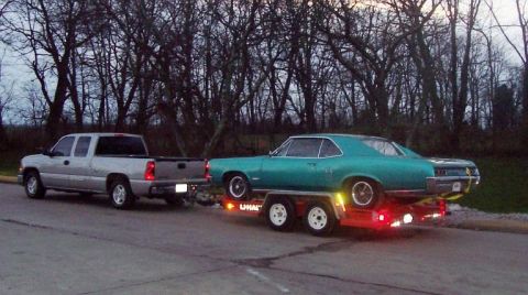 1967 Pontiac Lemans - A teal coupe is transported on a trailer behind a silver pickup truck on a cloudy day.