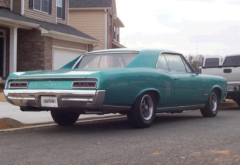Teal 1960s Pontiac coupe, rear 3/4 view, parked in driveway by a house.
