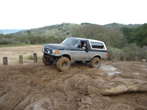 1989 Ford Bronco - A two-tone Ford Bronco navigates a muddy off-road course.