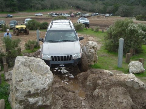 1989 Ford Bronco - A Jeep Grand Cherokee tackles a challenging muddy trail with other off-road vehicles visible.