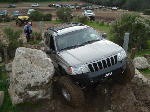 1989 Ford Bronco - A Jeep Grand Cherokee is shown attempting to traverse a rocky and muddy obstacle course.