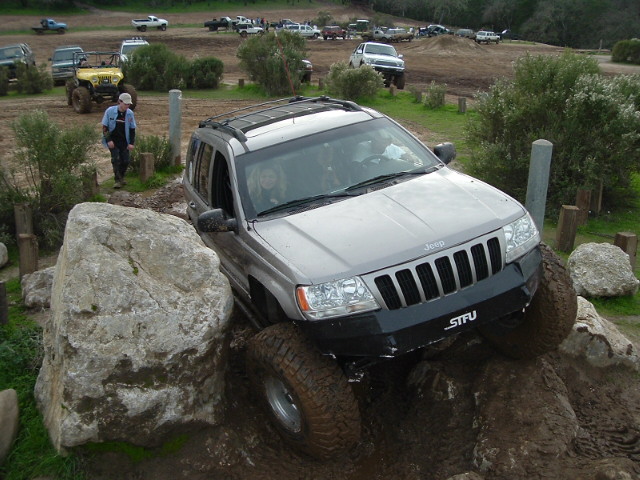 Silver lifted Jeep Grand Cherokee climbing rocks at an off-road park