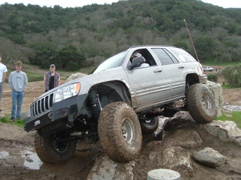 1989 Ford Bronco - A modified Jeep Grand Cherokee navigates a rocky obstacle course with onlookers present.