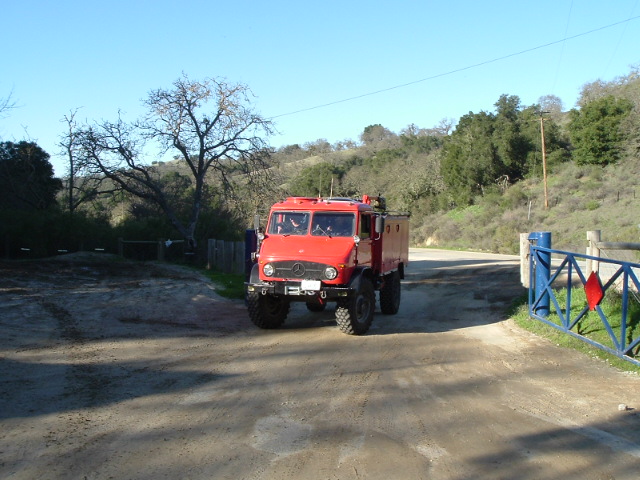 Red cab-over off-road truck on a dirt road in a rural hillside setting