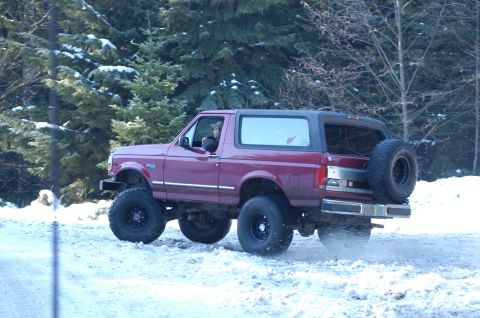 1995 Ford Bronco - Maroon Ford Bronco with a lifted suspension drives through a snowy, wooded area.