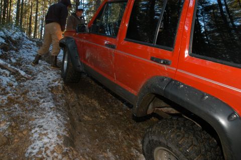 1995 Ford Bronco - Jeep Cherokee XJ navigating a difficult off-road trail in a wooded area.