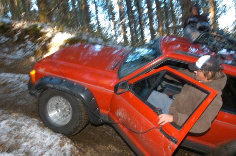 1995 Ford Bronco - A red SUV is navigating a snowy, wooded trail with a person in the driver's seat and another on the roof rack.