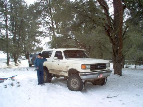 1988 Ford Bronco - A person stands next to a white Ford Bronco in a snowy, wooded area with another vehicle in the background.