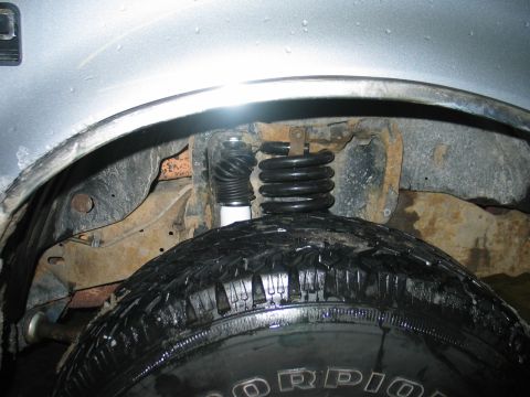 1995 Ford Bronco - Close-up view of the front suspension system, including the coil spring and shock absorber, positioned above the tire.