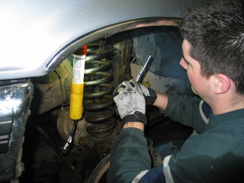 1995 Ford Bronco - Mechanic inspects a vehicle's suspension system, focusing on the coil spring and shock absorber.