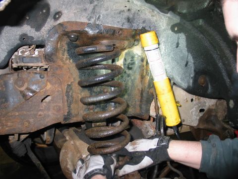 1995 Ford Bronco - A mechanic's gloved hands work on a heavily rusted suspension component, illuminated by a yellow flashlight.