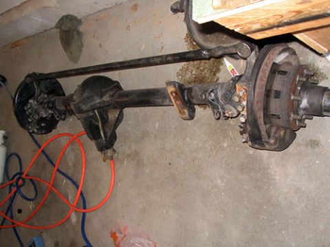 1995 Ford Bronco - A vehicle's rear axle assembly, including the differential, brake components, and driveshaft, rests on a concrete floor.